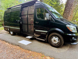 An Airstream Interstate RV rental is parked with its side door open, revealing a dog peering out from the camper van at a shady campsite.