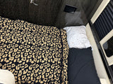 RV rental bedroom featuring a bed with a leopard print blanket, speckled pillow, and sleek dark interior finishes.