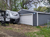 Silver RV rental travel trailer, supported on blocks, parked next to a grey garage with a white door.