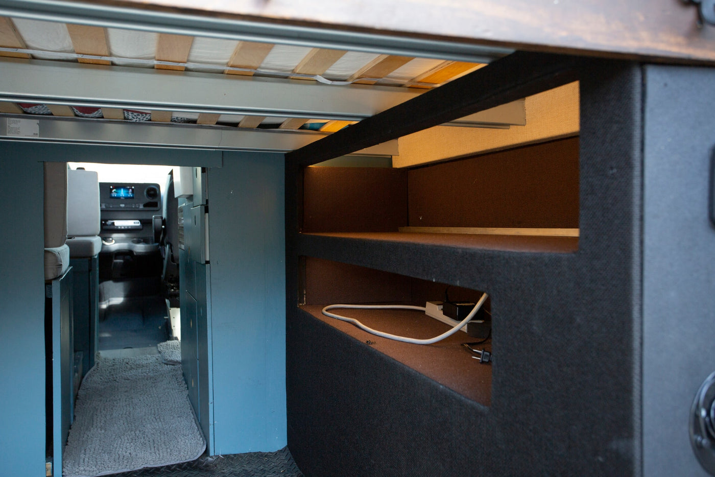 Explore this RV rental's interior: a raised bed, built-in storage with power outlets, and a clear view into the driver's cabin. — photo 18