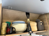 Inside an RV rental: a neat kitchen cabinet with bowls, mugs, utensils, and containers for organized travel.