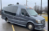 Grey Mercedes Sprinter van, customized as an RV rental, parked on asphalt. Features large tinted windows and roof units.