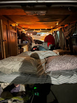 Cozy RV rental interior with a comfortable bed, warm string lights, and a person in the camper living space.