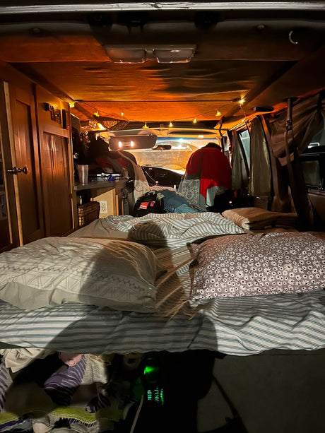 Cozy RV rental interior with a comfortable bed, warm string lights, and a person in the camper living space.