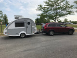 A red SUV tows a sleek grey teardrop RV rental, parked in a scenic campground ready for adventures.