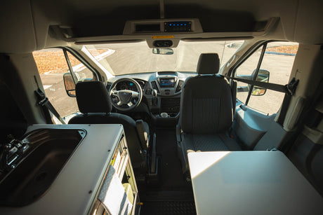Inside an RV rental camper van, showing the front cockpit, driver and passenger seats, and a built-in sink.
