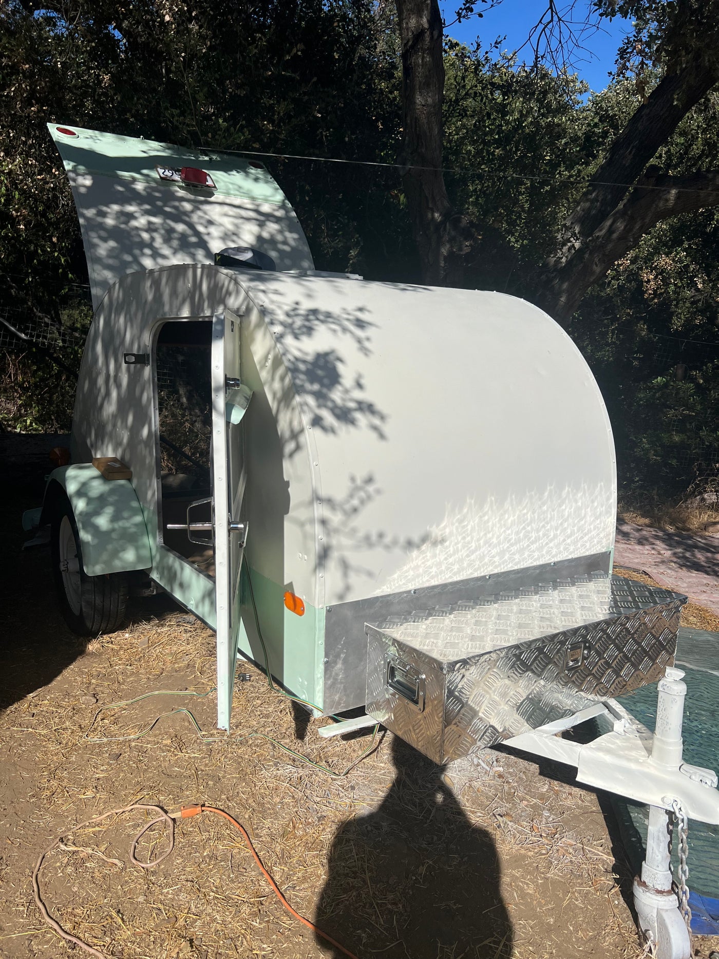 Teardrop RV rental: A compact, light green and white travel trailer with open doors and a front storage box, parked under trees. — photo 5