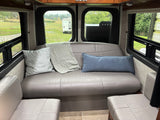 Cozy gray leather seating area in an RV rental, offering scenic views of a field and another RV from the windows.