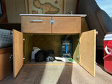 Custom RV rental interior with open cabinets reveals a water system for the sink, storage bags, and a dustpan.