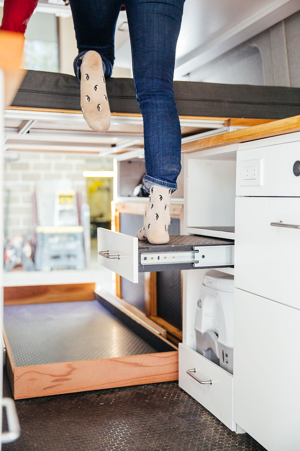 Climbing into the elevated bed of an RV rental, showcasing clever pull-out storage and a compact hidden toilet.