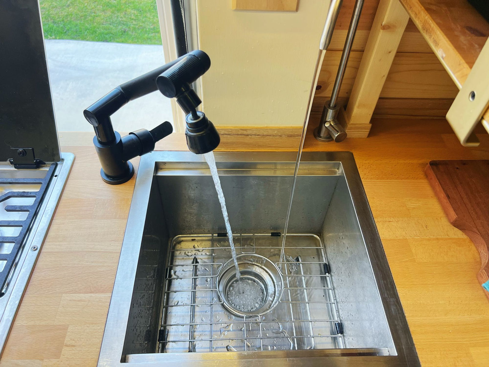 Inside an RV rental, a compact kitchen features a modern black faucet, stainless steel sink with running water, and wood counters.