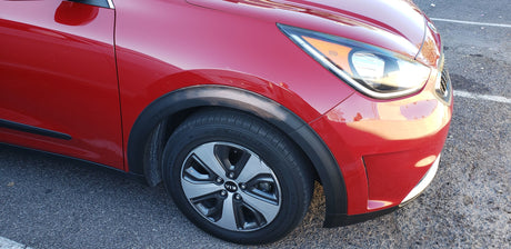 Red Kia Niro compact car, front view. Clear headlight, alloy wheel, tire visible. Not an RV rental, but a great travel vehicle.