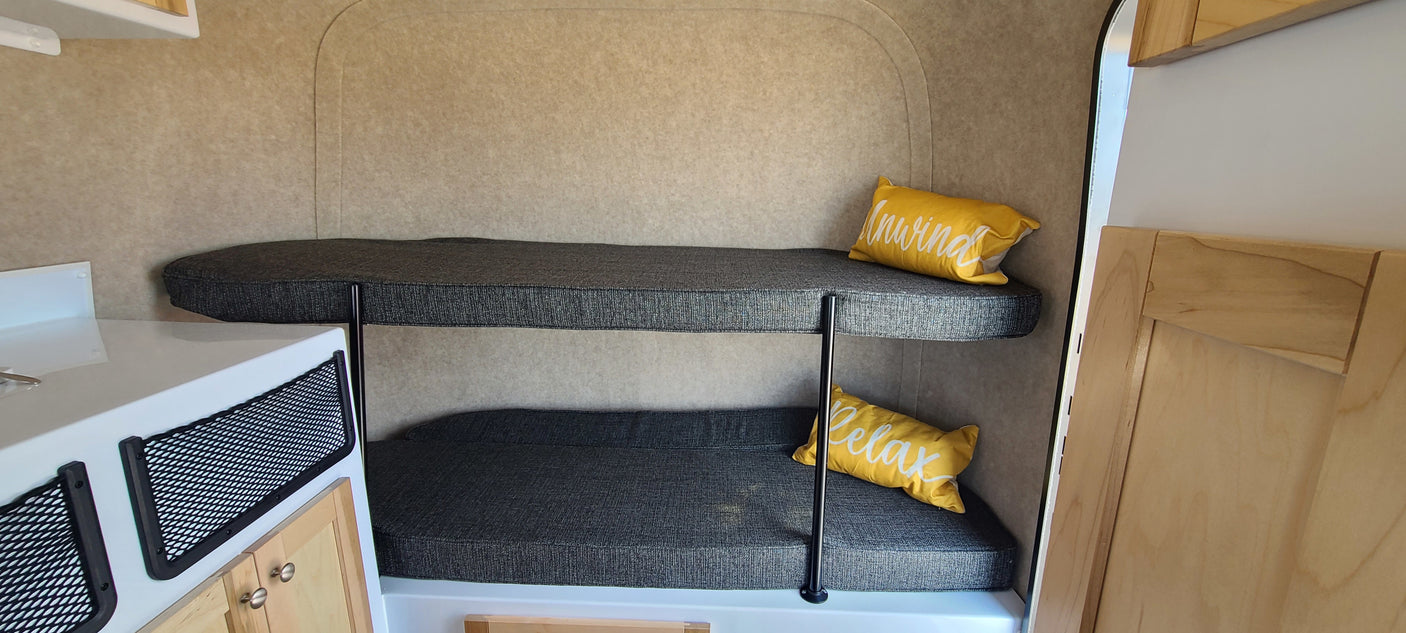 Compact RV rental interior: dark grey bunk beds with "Unwind" & "Relax" pillows, practical storage nets, and wooden cabinetry.