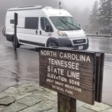 An rv rental, a white camper van, parked at the North Carolina/Tennessee state line in Great Smoky Mountains NP on a foggy day.