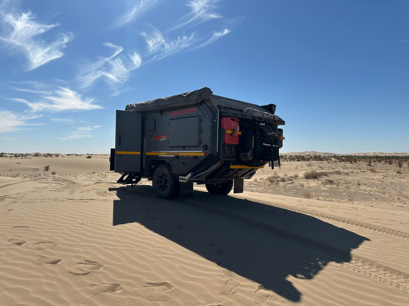 Rugged Conqueror off-road camper trailer on desert dunes, perfect for your next RV rental adventure. Clear blue sky, sand tracks. — photo 10