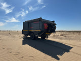 Rugged Conqueror off-road camper trailer on desert dunes, perfect for your next RV rental adventure. Clear blue sky, sand tracks.