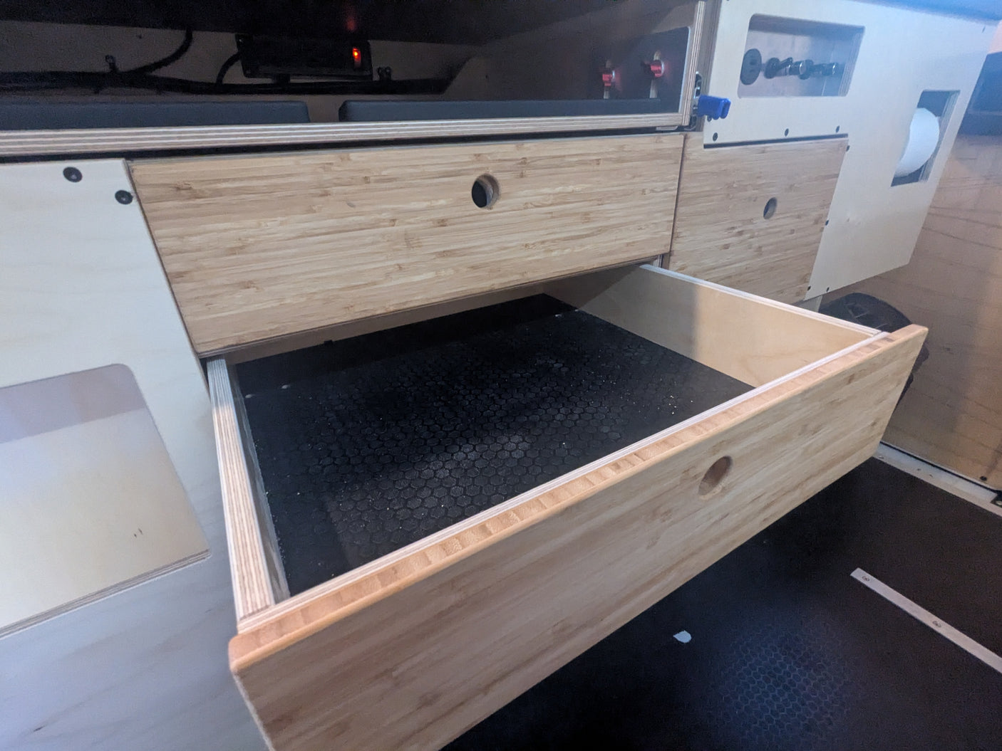 RV rental interior showing a smart wooden drawer, lined with a hexagonal mat, pulled open within modular cabinetry.