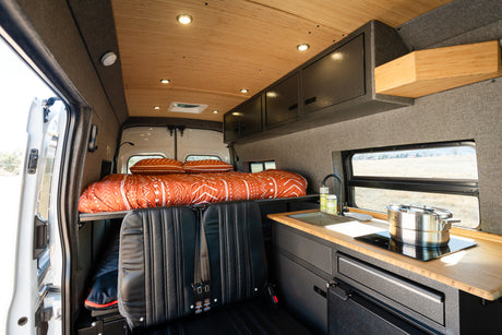 Cozy RV rental interior with a comfortable bed, compact kitchen, seating, and ample storage for mobile living.