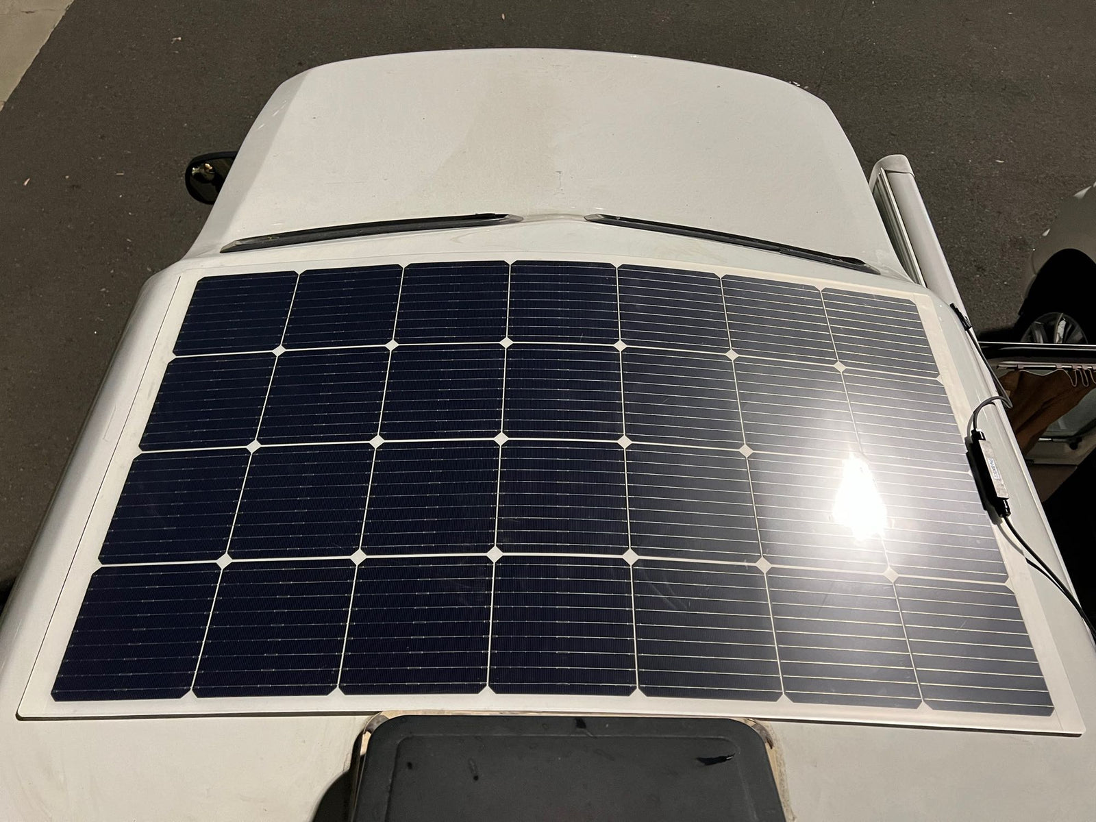 Overhead view of a white RV roof with a large, dark solar panel. Ideal for an RV rental offering off-grid power.