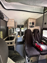Inside an rv rental campervan: kitchen, control panels, and seats with a child booster. Textured floor visible.