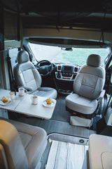 RV rental interior: Swiveled front seats form a cozy dining area with a table, coffee mugs, and muffins, perfect for travel.