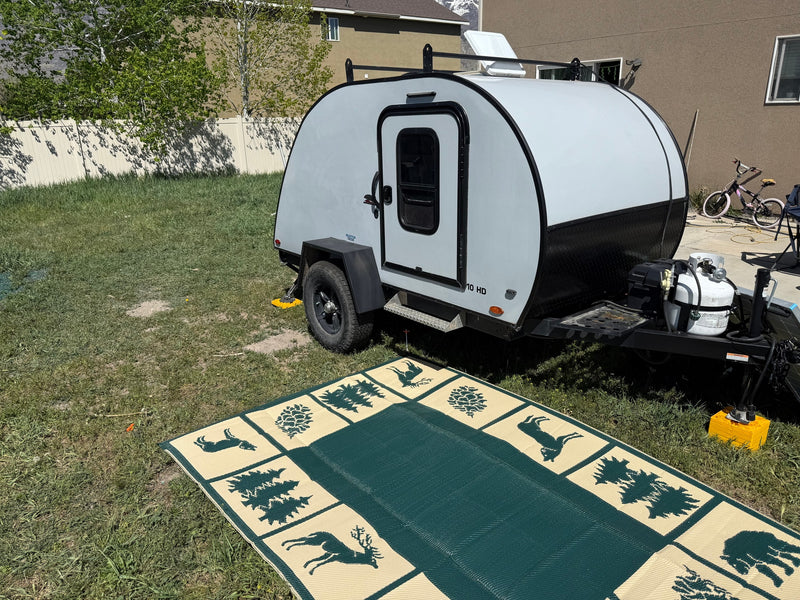 Light gray teardrop camper parked on grass with outdoor mat. Perfect for an RV rental adventure. — photo 2