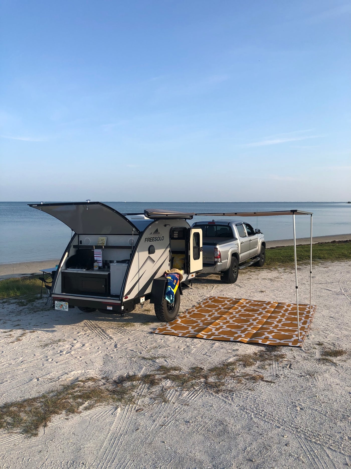 Beach camping setup with an RV rental & truck. Open camper kitchen, mat on sand by the ocean under clear skies. — photo 12