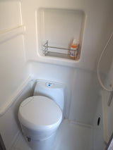 Compact RV rental wet bath with toilet, shower, and wall-mounted rack for toiletries, ideal for travel.