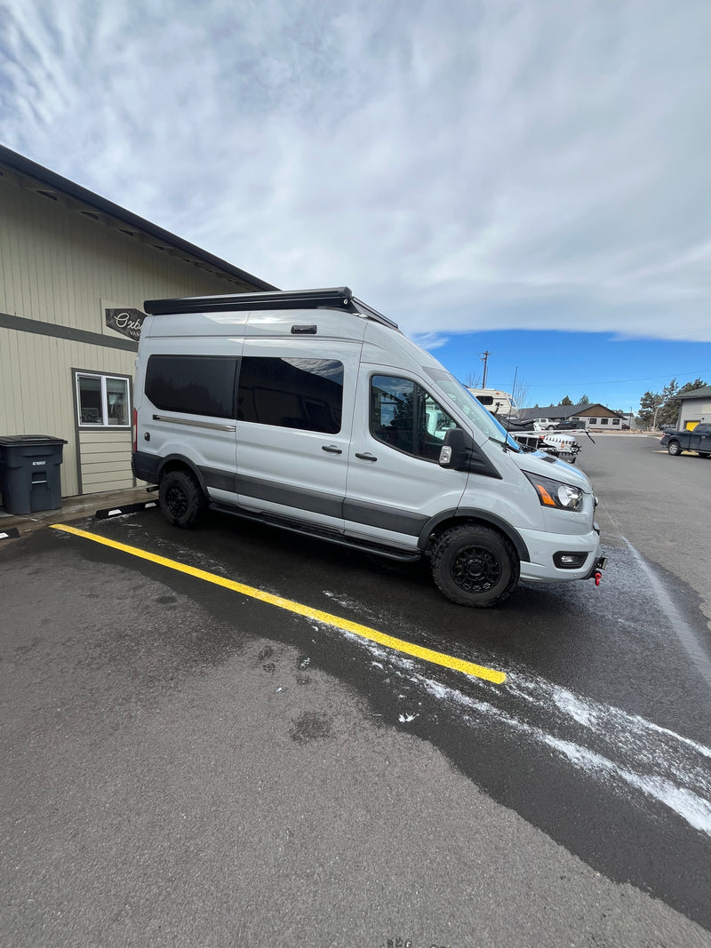 Light gray Ford Transit van (RV rental) with black wheels & roof awning, parked on an asphalt lot. — photo 5