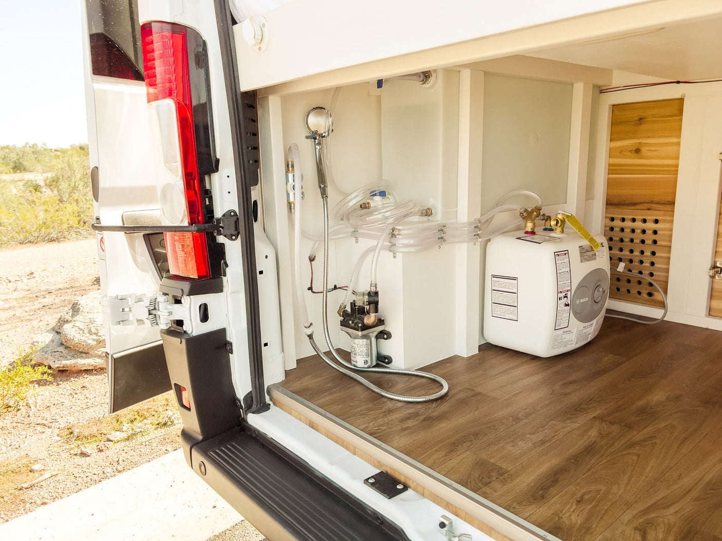 Rear access of an RV rental showing a compact water system setup with shower & Bosch water heater, ready for off-grid use.