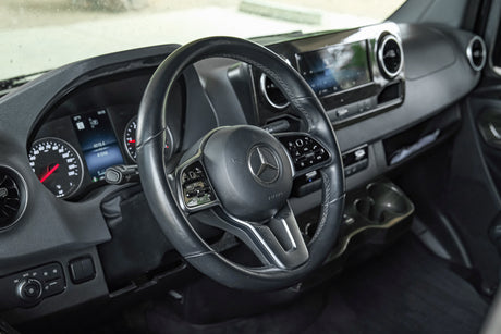 Driver's perspective inside a modern RV rental, showing the Mercedes-Benz dashboard, steering wheel, and instrument cluster.