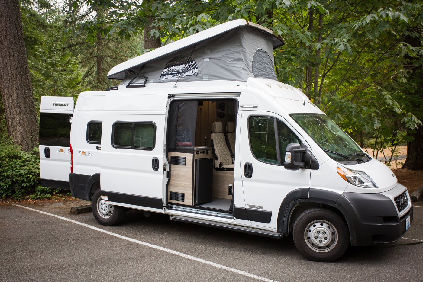  framed by a majestic waterfall cascading down granite cliffs with lush trees.|White Winnebago Solis camper van with pop-top extended and interior visible — photo 2