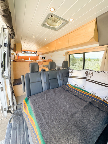 Explore van life with this RV rental's spacious interior: custom bed, versatile seating, and sleek wood storage.