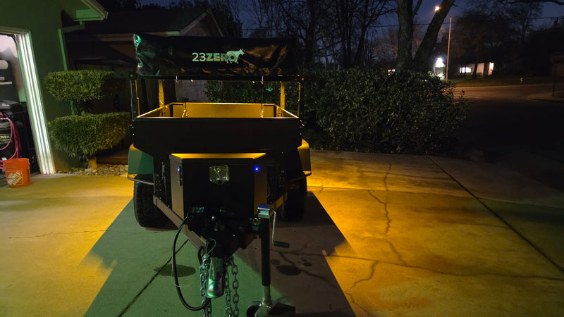 Night shot of a 23ZERO adventure trailer with tent cover, warmly lit on a driveway. Ready for camping or your next rv rental adventure. — photo 12