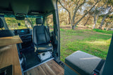 Inside a custom **rv rental** van, a spacious interior with wood accents & seating opens to a sunny, tree-filled natural setting.