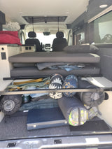 RV rental interior: A cozy camper van features a convertible bed, under-bed storage packed with gear, and visible power outlets.