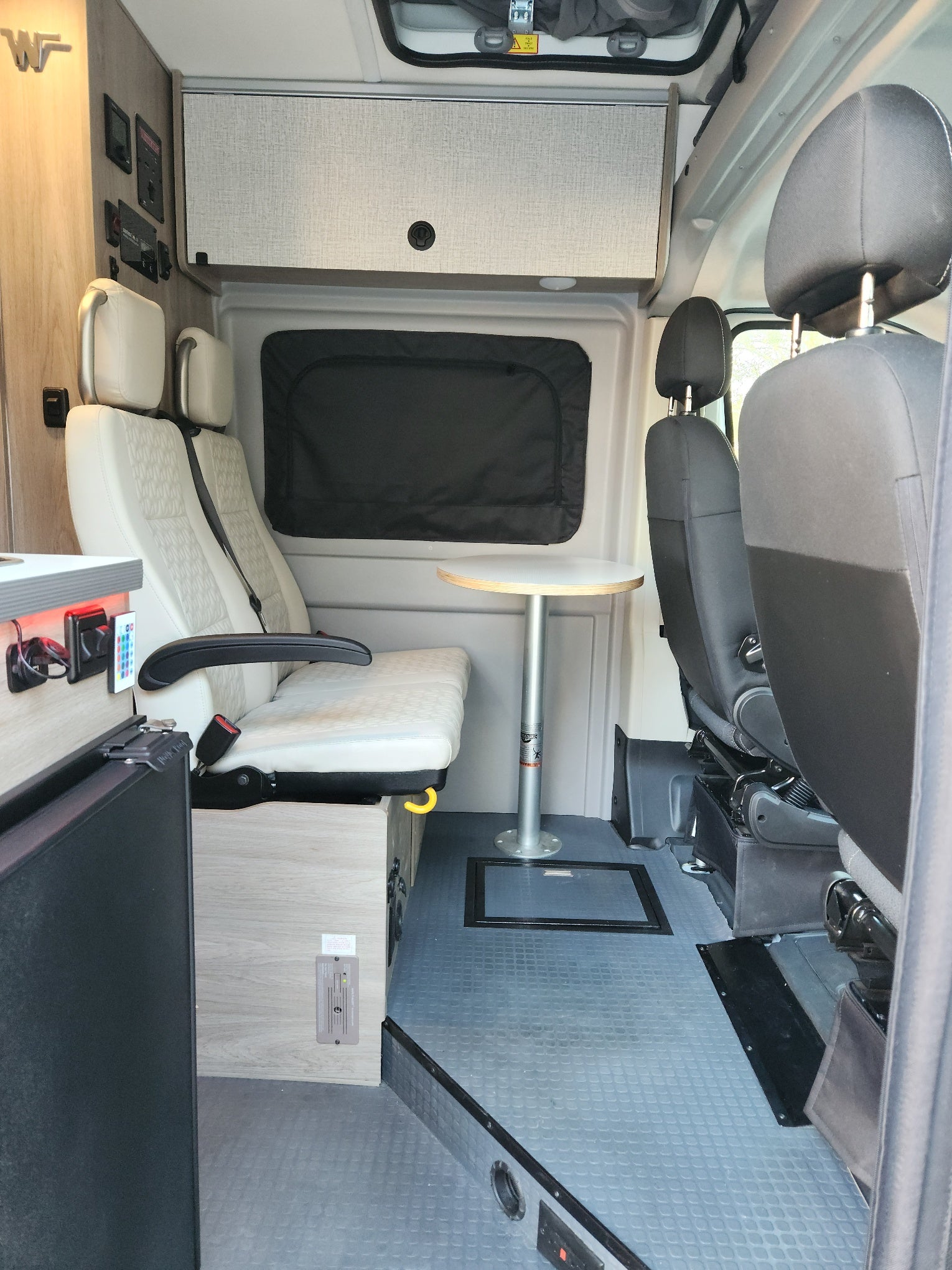 Spacious RV rental interior featuring comfortable passenger seats, a small table, and overhead storage for travel.
