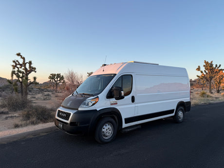 White Ram ProMaster campervan RV rental among Joshua Trees, perfect for desert road trips.