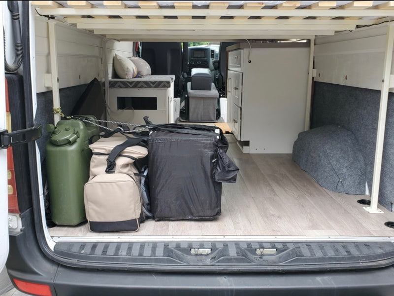 RV rental: Camper van interior features elevated bed, under-bed storage, a water can, and built-in cabinet. — photo 12