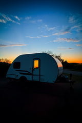 Cozy rv rental parked at sunset, glowing inside under a vibrant blue and orange sky. Ideal for a serene camping adventure.