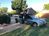Minivan with rooftop tent and awning set up like an RV rental. Child smiles from tent in sunny campground.