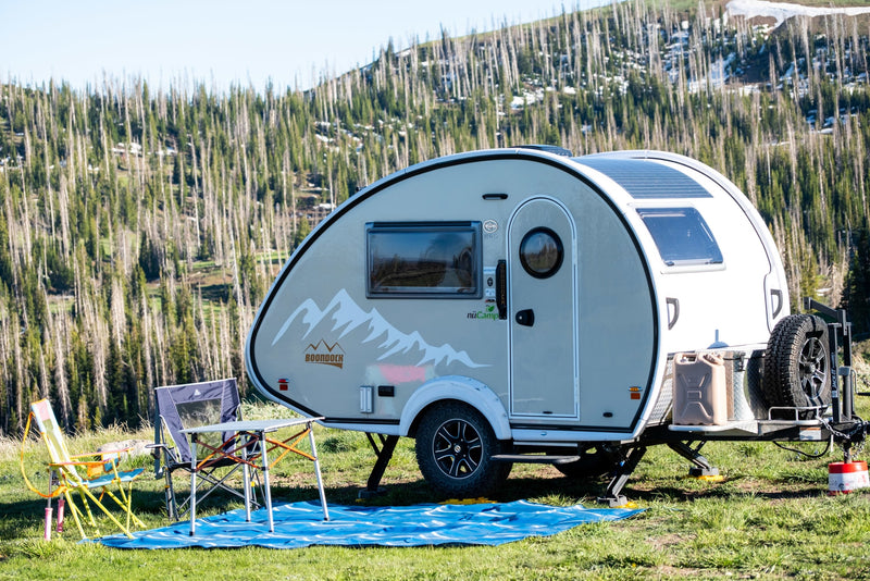 This nuCamp Boondock teardrop rv rental is set up for camping, with solar panels, chairs, and a table in a mountain forest. — photo 1
