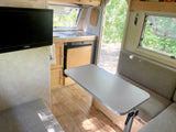 Interior of an RV rental: compact kitchen with sink, dining table, and television on the left.