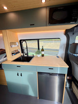 Modern RV rental kitchen with sink, microwave, fridge, and stylish teal cabinets for comfortable travel.
