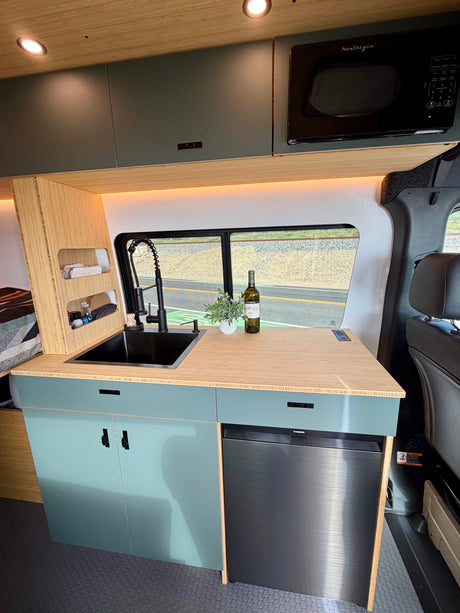 Modern RV rental kitchen with sink, microwave, fridge, and stylish teal cabinets for comfortable travel.