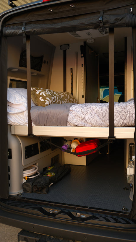 RV rental interior: elevated bed with bedding, under-bed storage with a hose and mesh net, ideal for camper van trips.