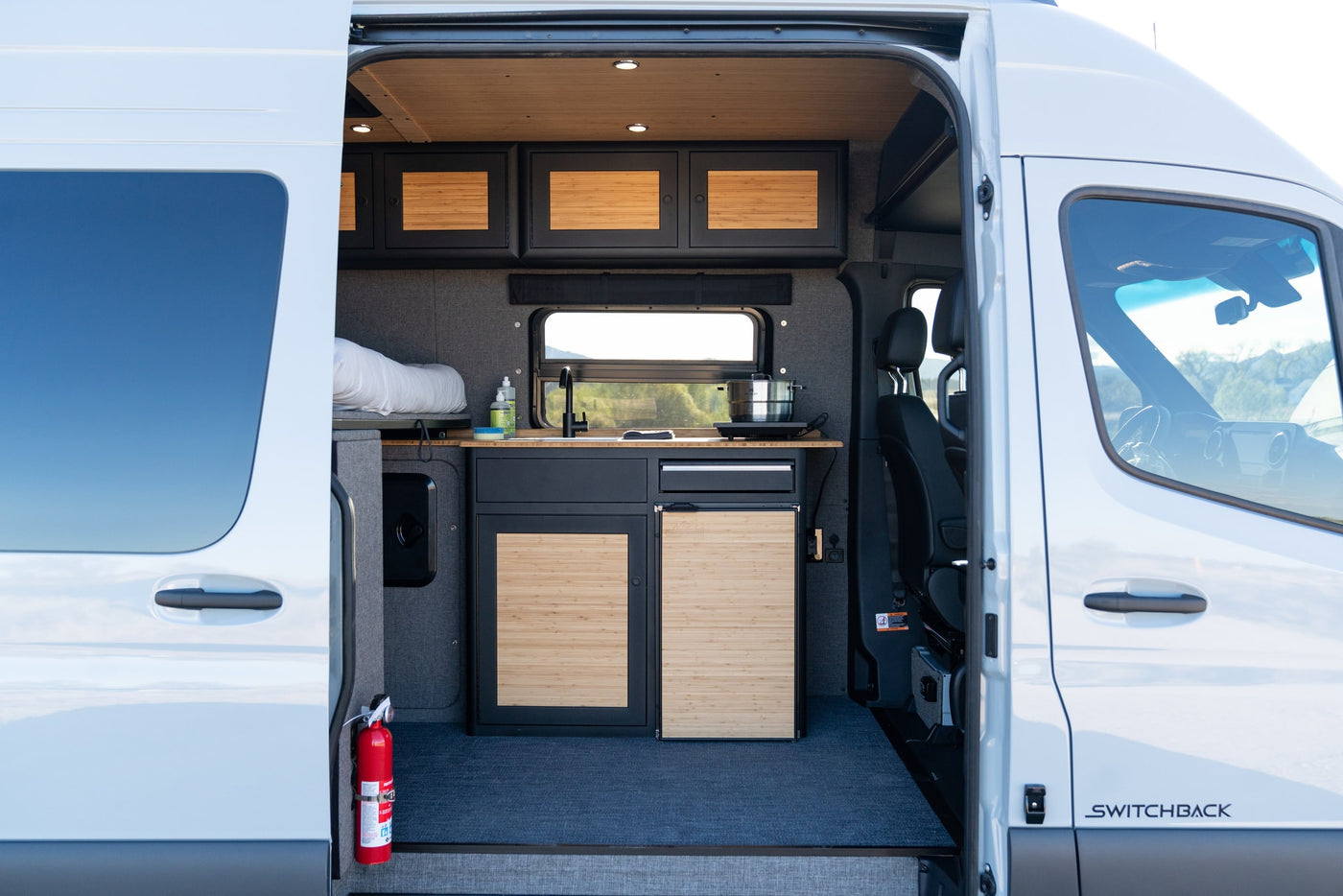 View inside an rv rental camper van, revealing its modern interior with a compact kitchen, bed, and bamboo cabinets. — photo 8