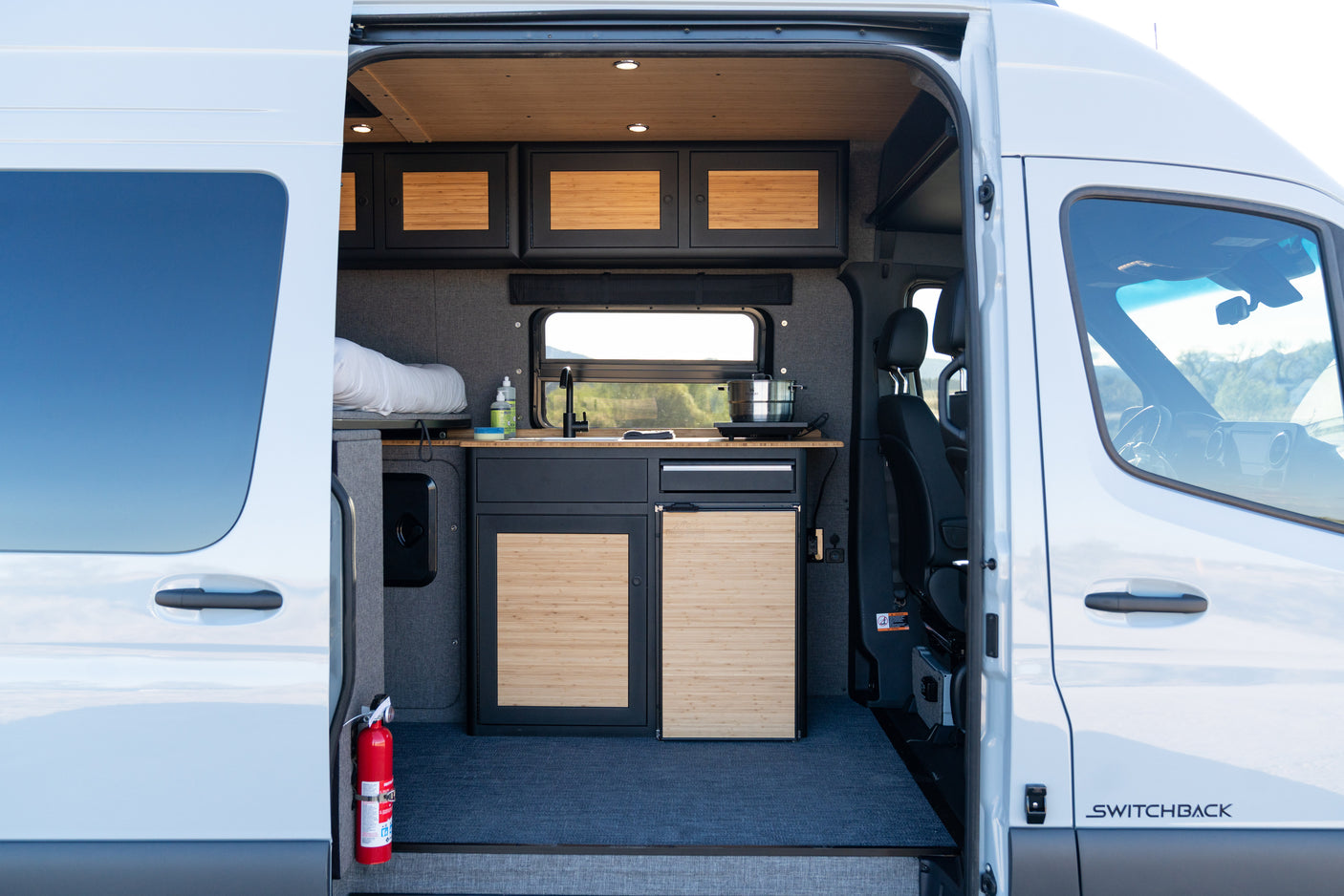 View inside an rv rental camper van, revealing its modern interior with a compact kitchen, bed, and bamboo cabinets.
