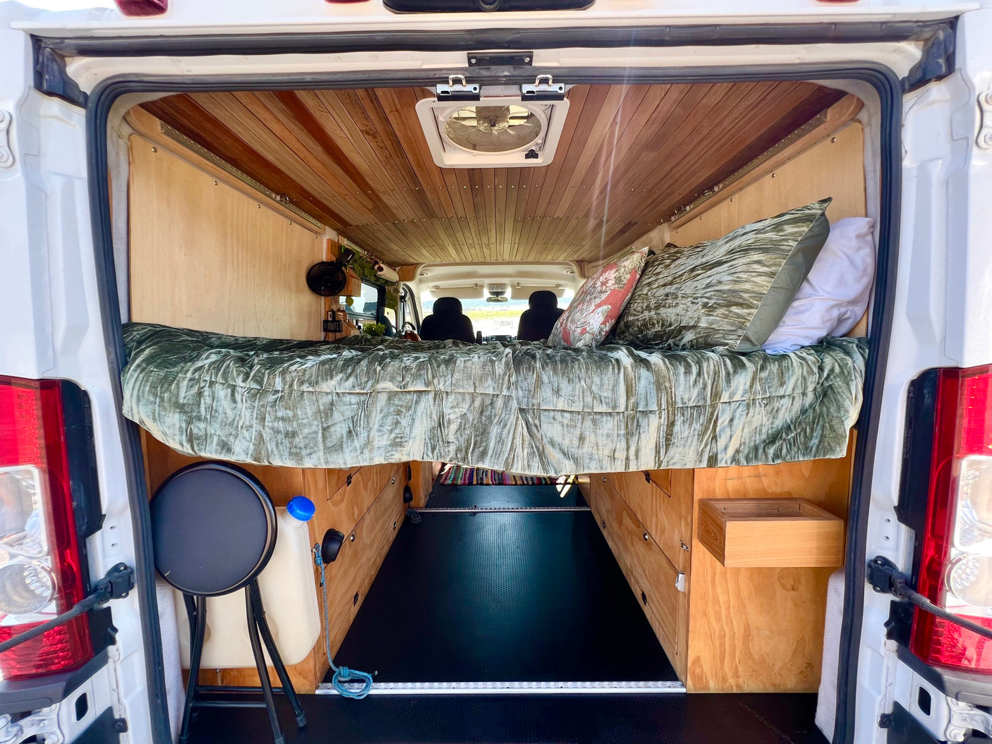 Cozy RV rental: Inside a custom campervan showing a raised bed with velvet bedding, wood ceiling, and under-bed storage space.