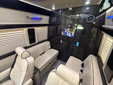 Plush, cream-colored quilted seating, dark wood interior, and TV inside this luxurious van, ideal for your next RV rental.